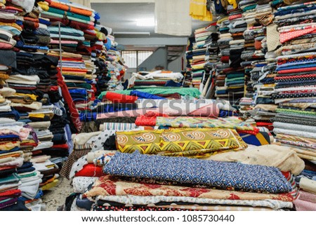 Fabric, colorful variety of rolls stacked in shelves and also on a central table inside a store.