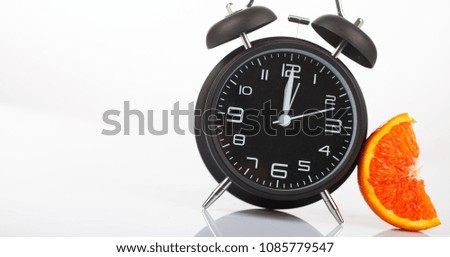 Old vintage black alarm clock near green barbell and two half of orange with yellow meter on studio white background