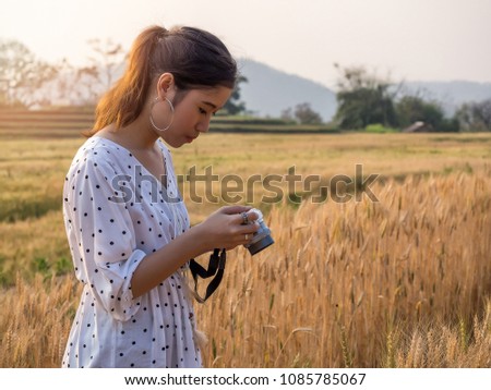 Young woman taking photograph a ladybug perched on grains of barley in a field of barley.
