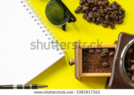top view flat lay coffee hipster life style set, coffee beans, grinded beans in vintage wooden coffee grinder, blank book  and sun glasses on yellow modern background