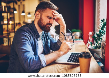 Overwhelmed bearded young man freelancer forgot to make money transaction during distance job at modern netbook device.Tired skilled student has headache because of overworking at laptop computer Royalty-Free Stock Photo #1085823935