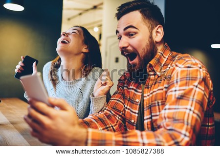 Excited male and female hipsters rejoice in winning an internet lottery made bets on website on modern smartphone.Happy couple in love celebrating victory in online competitions enjoying success Royalty-Free Stock Photo #1085827388