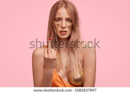 Candid shot of discontent adorable young woman decorated with spangles, poses against pink background. Body language, artistic make up and beauty concept