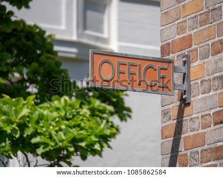 Office sign posted on a brick building outdoors on a sunny day