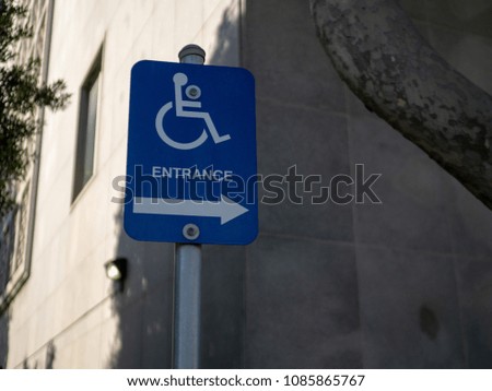 Handicap entrance sign pointing to the right in a sunny outdoor area