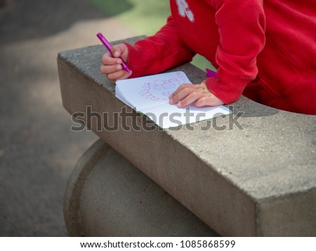 Child drawing pictures in paper notebook in a park outside