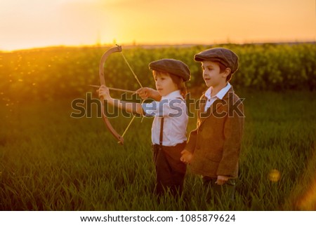 Portrait of children playing with bow and arrows, archery shoots a bow at the target on sunset Royalty-Free Stock Photo #1085879624