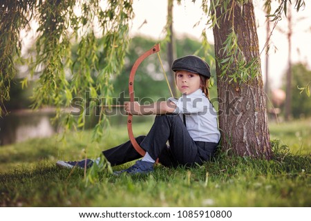 Portrait of child playing with bow and arrows, archery shoots a bow at the target on sunset Royalty-Free Stock Photo #1085910800