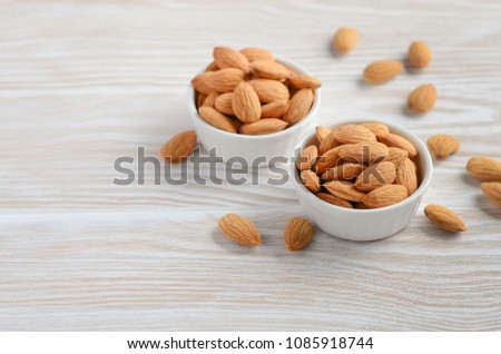Almonds in a bowls on a white wooden background, selective focus, copy space.