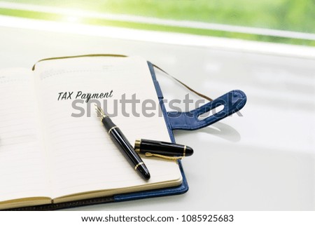 pen and notebook with TAX Payment word on the white table near window, sideview with green light backgrounds