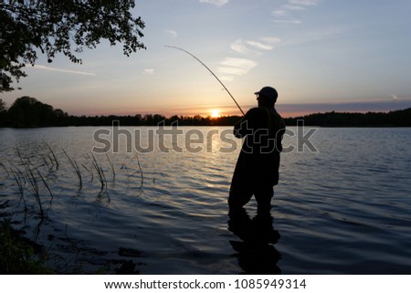 Silhouette of fisherman standing in the lake and catching the fish during sunset
