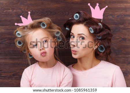 young mother and daughter with hair curlers having fun together and holding paper crown