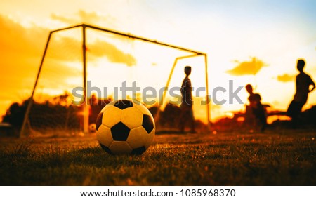 An action picture of a group of kids playing soccer football for exercise in community rural area under the sunset.