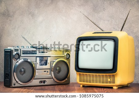 Retro old designed tube TV receiver and ghetto blaster stereo radio cassette tape recorder boombox from circa late 70s front concrete wall background. Vintage nostalgia style filtered photo