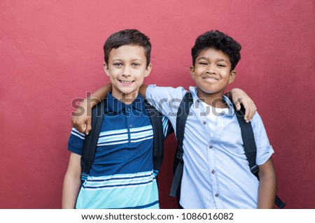 Best children friends standing with hand on shoulder against red background. Happy smiling classmates standing together on red wall. Portrait of multiethnic schoolboys enjoying friendship. Royalty-Free Stock Photo #1086016082