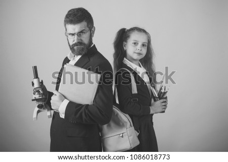 Teacher and schoolgirl with proud faces on orange background. Girl and man in suit and school uniform. Kid and tutor hold microscope, book and stationery. Classroom and alternative education concept