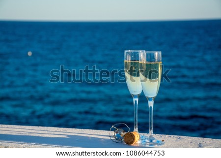 Two glasses with champagne or cava sparkling wine served outside on terrace with pink exotic flowers, luxury resort with sea view, romantic vacation