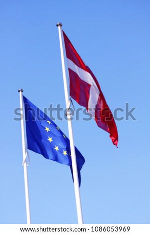 European Union EU and danish flag for Denmark on a pole waving in the wind with a blue sky on a sunny day as background