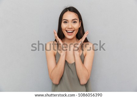 Portrait of an excited asian woman looking at camera and laughing isolated over gray background
