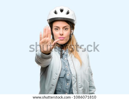 Young woman with bike helmet and earphones annoyed with bad attitude making stop sign with hand, saying no, expressing security, defense or restriction, maybe pushing