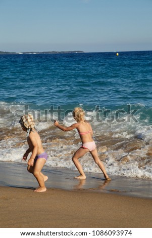 Little girl and boy playing with waves on the beach