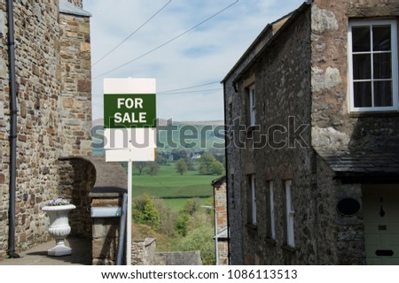 Green And White For Sale Sign With Idyllic Countryside Background On Street Of Beautiful Stone Houses