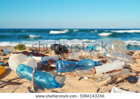 Spilled garbage on the beach of the big city. Empty used dirty plastic bottles. Dirty sea sandy shore the Black Sea. Environmental pollution. Ecological problem. Moving waves in the background Royalty-Free Stock Photo #1086143246