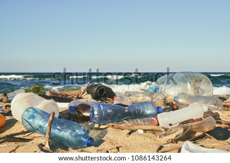 Spilled garbage on the beach of the big city. Empty used dirty plastic bottles. Dirty sea sandy shore the Black Sea. Environmental pollution. Ecological problem. Moving waves in the background Royalty-Free Stock Photo #1086143264