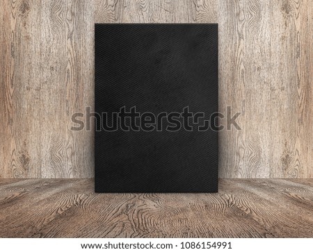 Blank black canvas poster leaning at wood wall on wooden floor in perspective room,Business mock up presentation.Template display of design or content