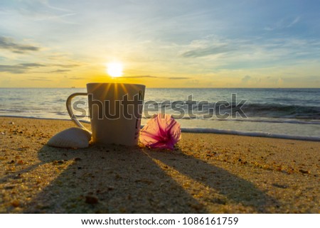 A coffee cup on sand with flower and shell at sea in the morning