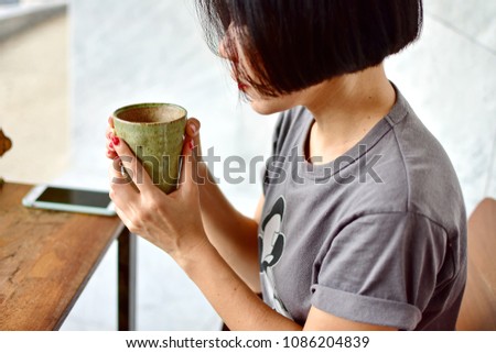Young woman short hair style will sipping  hot tea or coffee in green ceramic cup have smartphone on wooden table blurred background, slow life in lifestyle of new generation concept