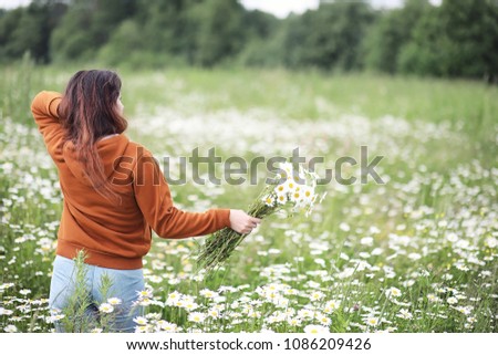 Beautiful girl collects daisies in summer day in afield
