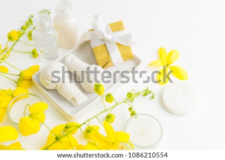 Bright spa background: candles, thai massage herbal bags, shampoo bottles, yellow flowers and gift box with ribbon on white. Health, skin treatment, holiday sale concept. Text space Royalty-Free Stock Photo #1086210554