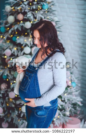 Beautiful pregnant woman in denim overalls holding a Teddy bear