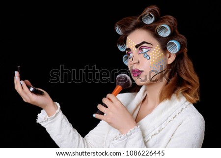 Model with comic pop art makeup looking to the mirror, posing against black background.