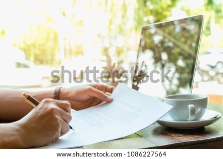 Businessman hand holding pen over agreement form with laptop and coffee on table
