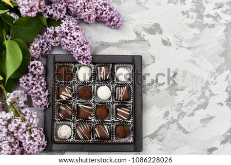 A box of chocolates on a gray background and lilac flowers. delicious chocolate candies