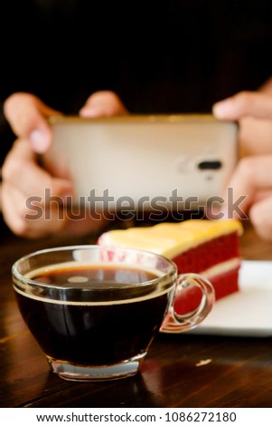 taking photo with black coffee and red velvet cake on dark wooden table with smartphone with man hand. for up to social network .