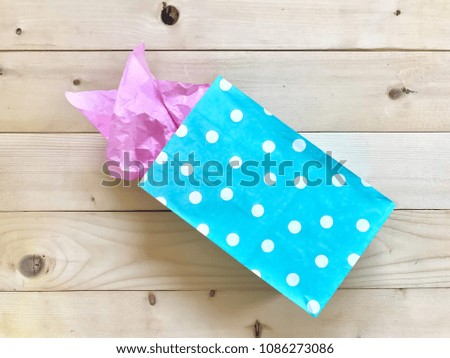 Closeup light blue colored polka dot gift bag with pink crumpled tissue paper on wooden board background. The concept of  Birthday celebration party. Top view with Copy space.Selective focus.