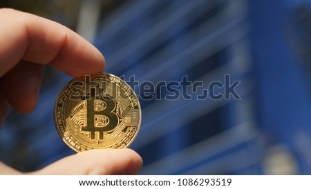 Hand holding Bitcoin gold coin and business building in the background