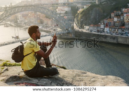 Traveler man doing photo on mobile phone. Porto, famous iron bridge and Douro rive on background 