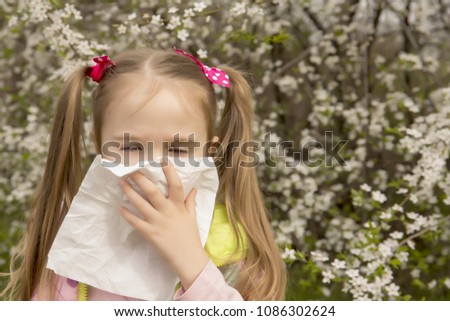 A little girl with an allergy sneezes against the background of flowering trees, in the spring