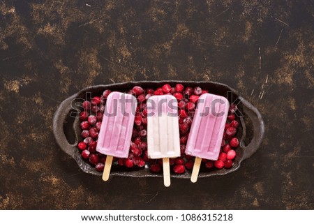 Berry ice cream on a stick of purple color with frozen berries on a ceramic tray. Top view, space for text