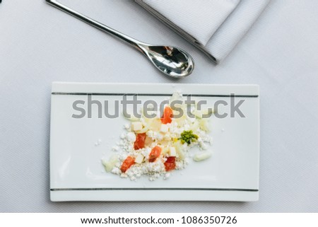 Modern French appetizer: crush and cut cheese with diced tomato served on white rectangle plate with silver spoon and napkin.
