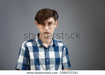 Portrait of a normal boy with round rimmed spectacles over grey background. Young man face, high detailed portrait. young attractive man in blue checkered shirt