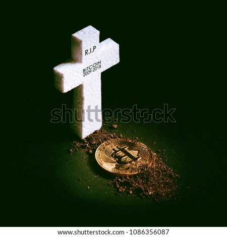 white grave cross and bitcoin sprinkled with earth. The concept of the fall of the cost of bitcoin and its death as the most expensive crypto currency