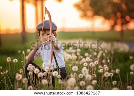 Portrait of child playing with bow and arrows, archery shoots a bow at the target on sunset Royalty-Free Stock Photo #1086429167