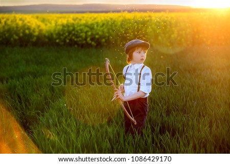 Portrait of child playing with bow and arrows, archery shoots a bow at the target on sunset Royalty-Free Stock Photo #1086429170