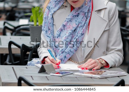 Beautiful young business woman sitting in an outdoor cafe and working with documents.