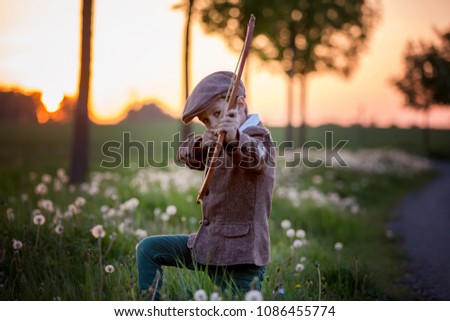 Portrait of child playing with bow and arrows, archery shoots a bow at the target on sunset Royalty-Free Stock Photo #1086455774